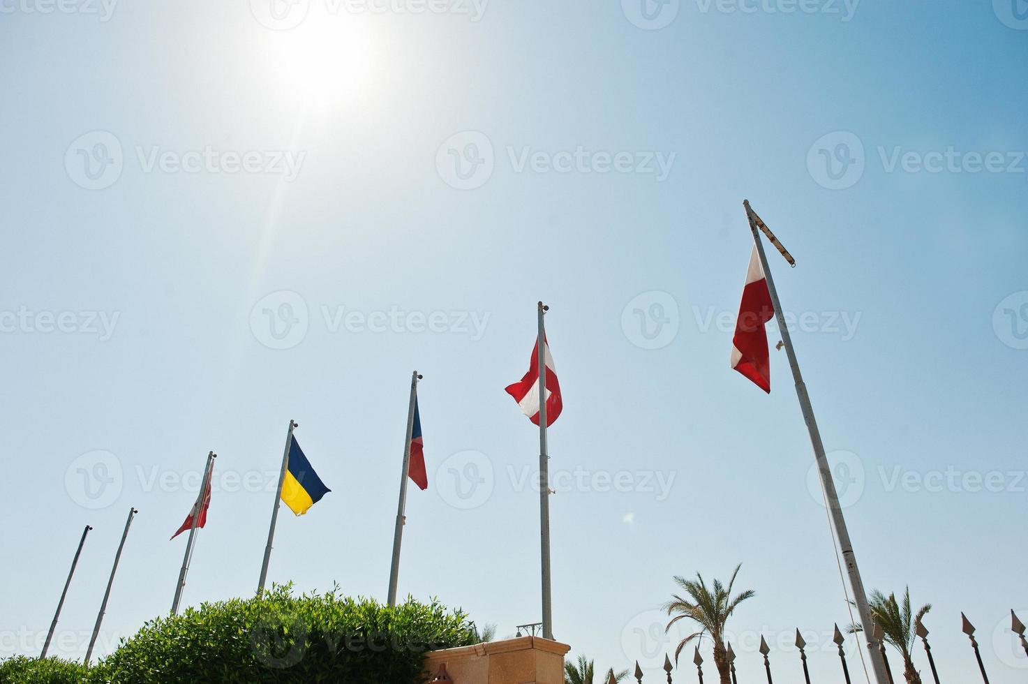 Staatsflaggen wehen im Wind an Fahnenmasten vor blauem Himmel mit Sonne foto