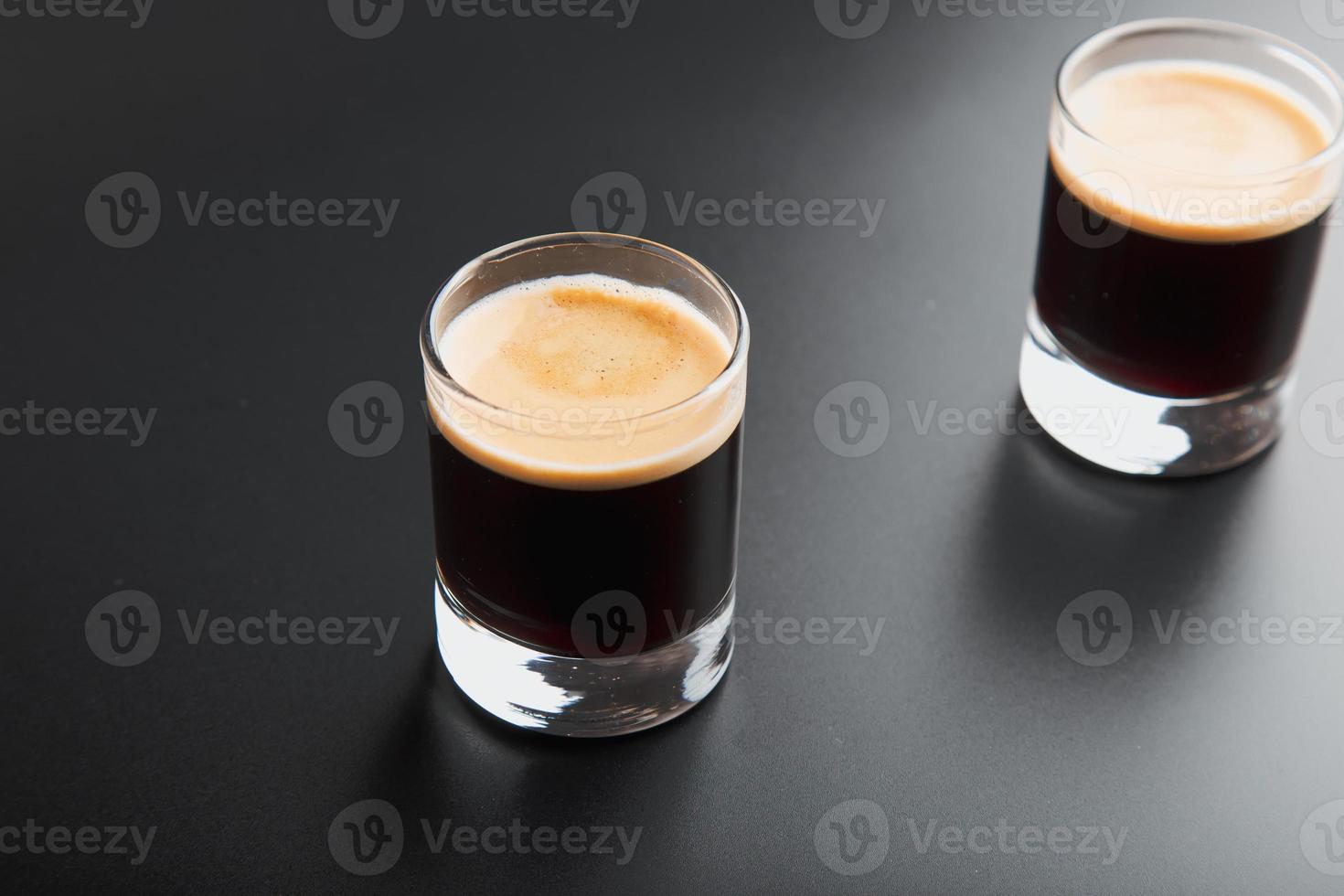 Detailansicht der Nahaufnahme von zwei Espresso-Schnapsgläsern über glänzendem, elegantem schwarzem Hintergrund mit Kopierraum. foto