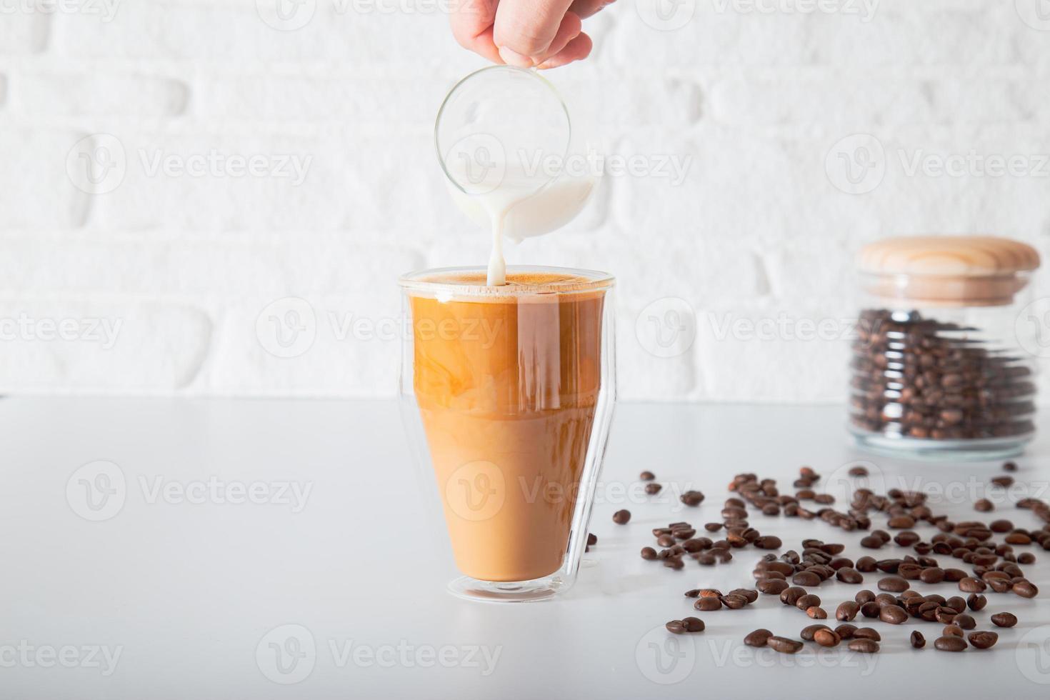 Eine anonyme Hand gießt Milch in ein doppelseitiges Glas Kaffee. foto
