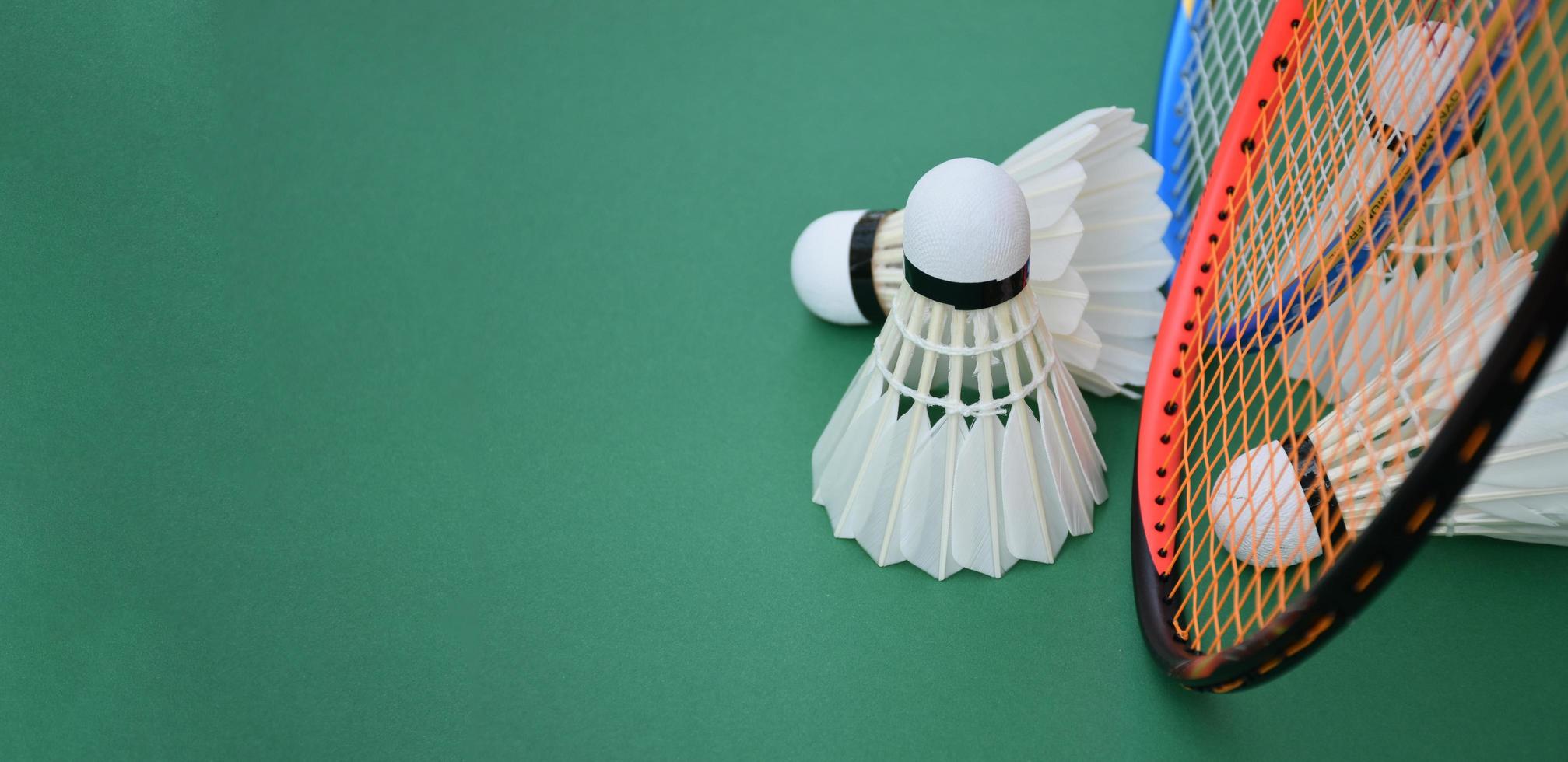 Cremeweißer Badmintonfederball und Schläger mit Neonlichtschattierung auf grünem Boden im Indoor-Badmintonplatz, verschwommener Badmintonhintergrund, Kopierraum. foto