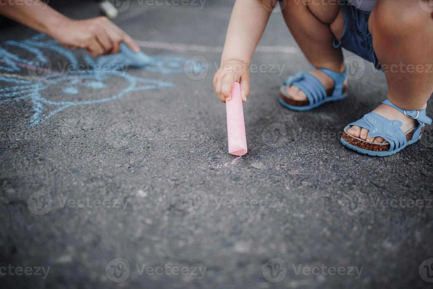 Nahaufnahme eines kleinen Mädchens, das mit Kreide auf dem Bürgersteig zeichnet foto