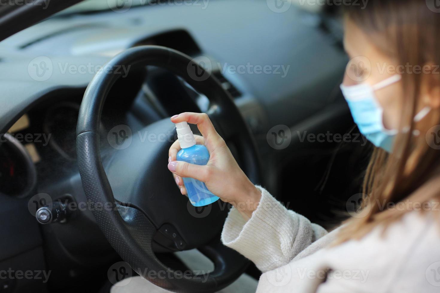 Sprühen von antibakteriellem Desinfektionsspray im Auto, Infektionskontrollkonzept. Desinfektionsmittel zur Vorbeugung von Coronavirus, Covid-19, Grippe. Sprühflasche. Frau, die eine medizinische Schutzmaske trägt, die ein Auto fährt. foto
