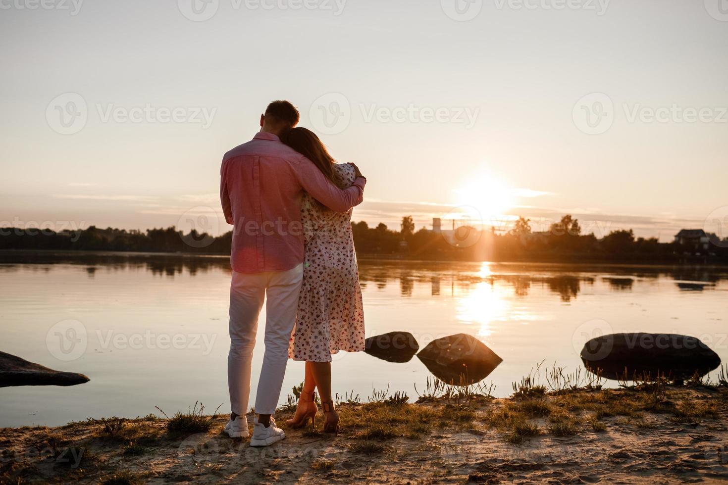 Paar umarmt sich bei Sonnenuntergang. Schönes junges verliebtes Paar, das bei Sonnenuntergang in den Strahlen des hellen Lichts am See entlang geht. selektiver Fokus. konzept von familie, komfort, sicherheit foto