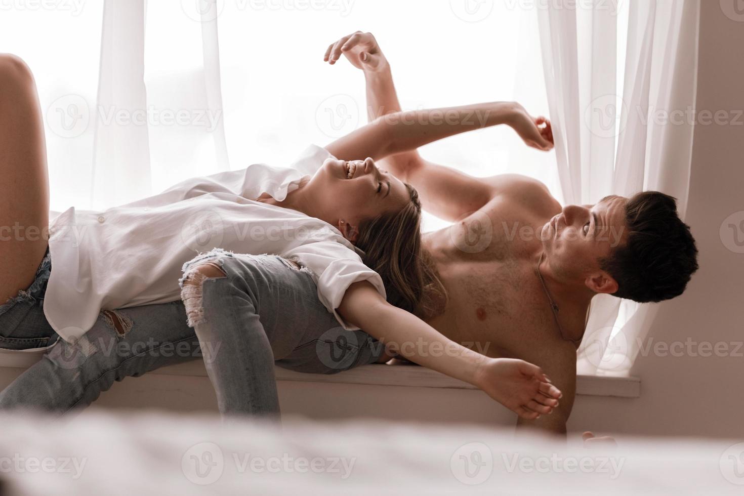 Liebespaar, das zu Hause Spaß hat, verspielte Frau, die lächelndes Ehemannohr beißt, Huckepack, Mann und Frau spielen kindisch im Bett und genießen lustige intime Momente foto