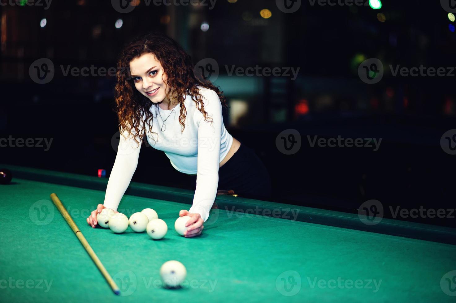 Junges lockiges Mädchen posierte in der Nähe eines Billardtisches. sexy Model im schwarzen Mini-Minirock russisches Snooker spielen. spiel und lustiges konzept. foto