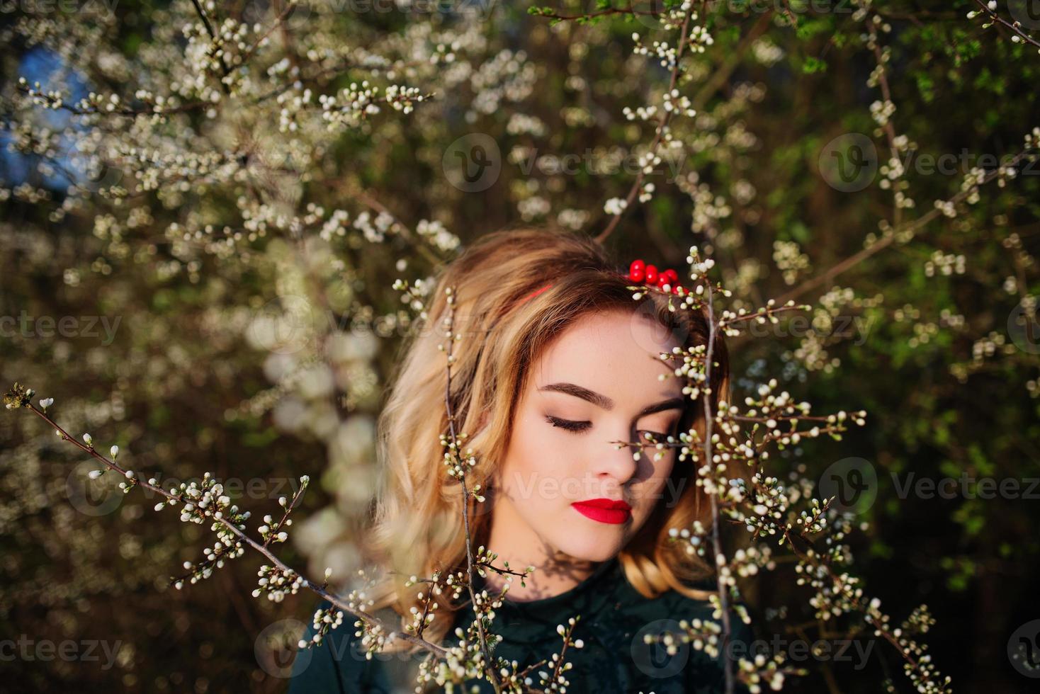 Nahaufnahme des Porträts des blonden Mädchens der Yong-Eleganz im grünen Kleid im Garten im Frühling auf blühenden Bäumen. foto