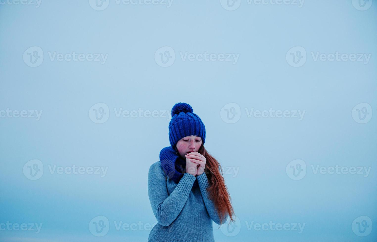 Porträt eines jungen Mädchens mit roten Haaren und Sommersprossen, das im Wintertag Hintergrundeis in blau gestrickter Wollmütze und Schal trägt. foto