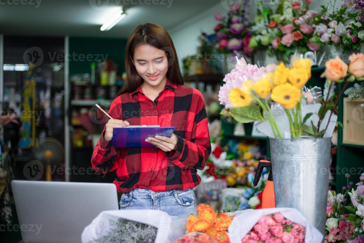 asiatische frau florist kleinunternehmen blumenladenbesitzerin und sie benutzt ihr telefon und ihren laptop, um bestellungen für ihr geschäft entgegenzunehmen. foto