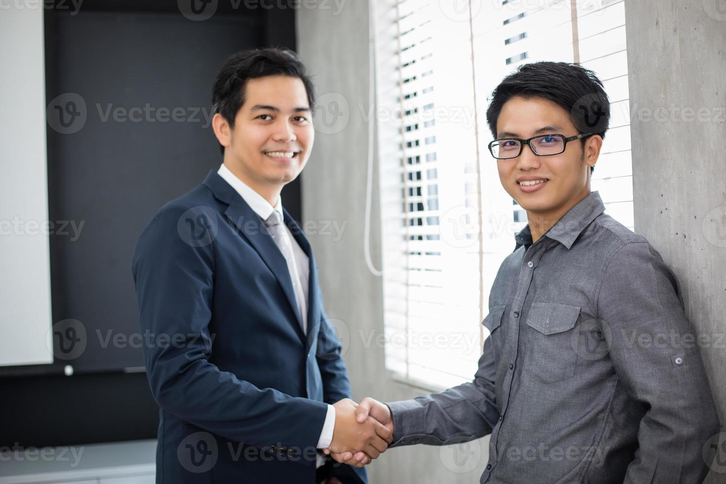 Asiatische Geschäftsleute, die sich die Hände schütteln und ihre Zustimmung zur Vertragsunterzeichnung und zum Abschluss eines Meetings lächeln foto
