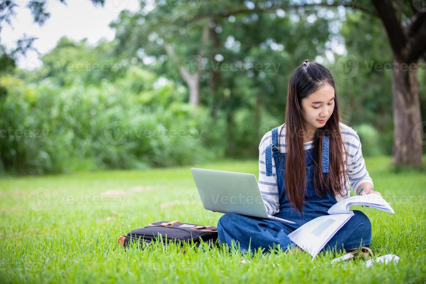 schöne asiatische studentin, die bücher hält und in die kamera lächelt und im sommer ein lern- und bildungskonzept im park zur entspannungszeit hat foto