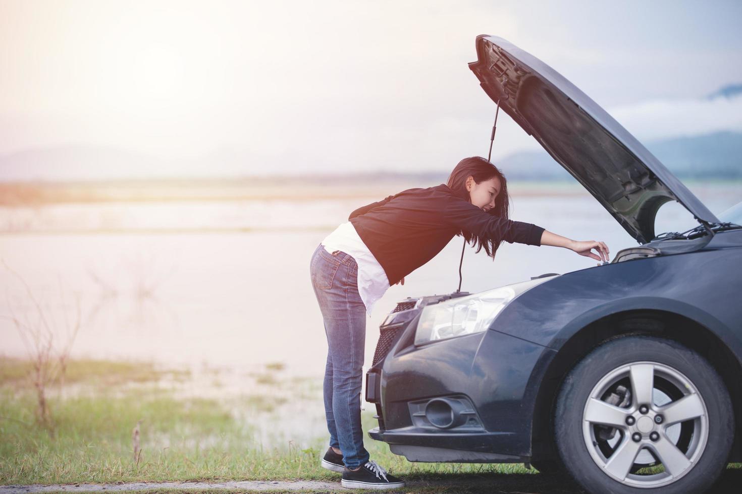 asiatische Frau, die ein kaputtes Auto auf der Straße überprüft foto