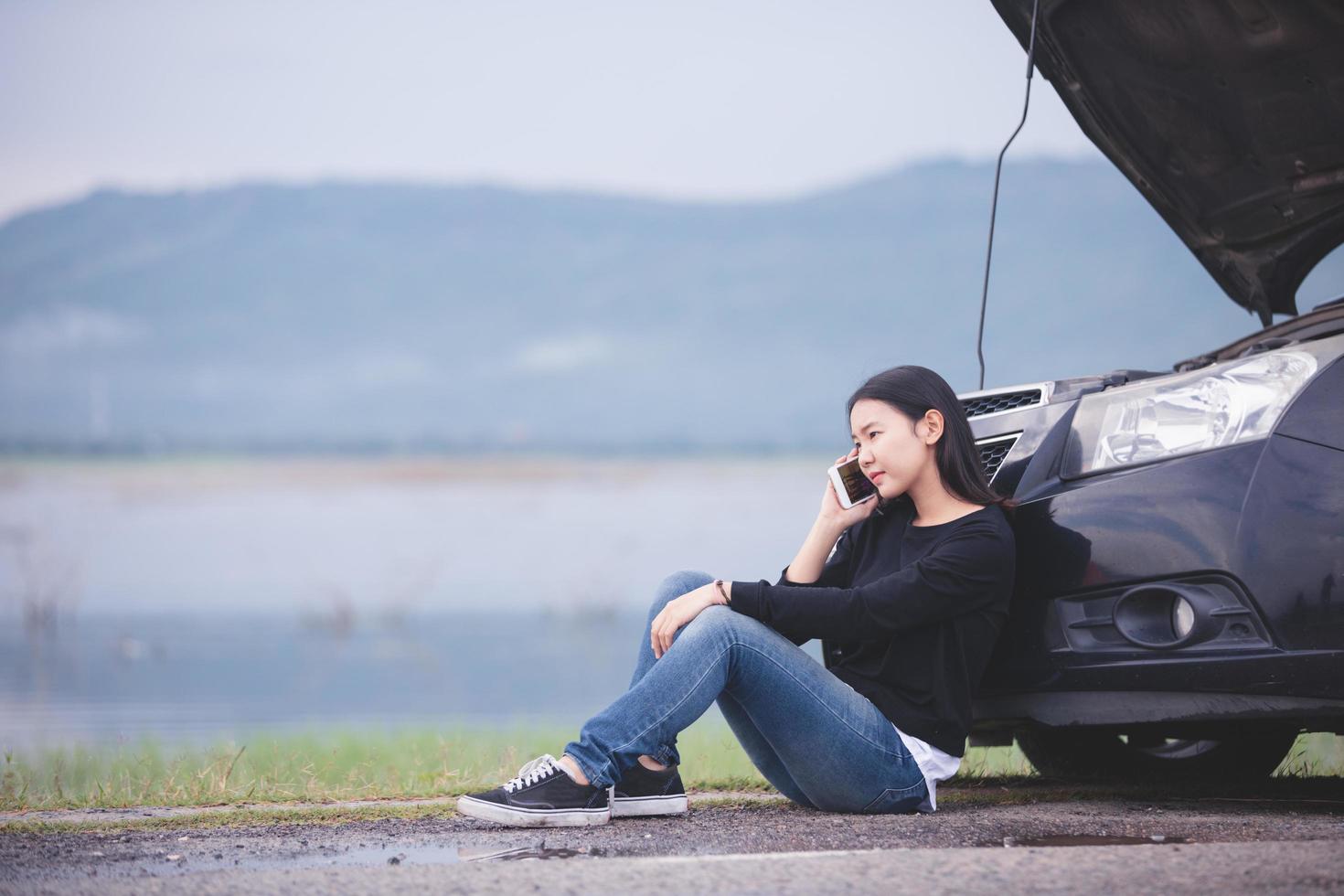 asiatische frau benutzt ein telefon, um den automechaniker anzurufen. zum Reparieren beschädigter Autos auf der Straße foto