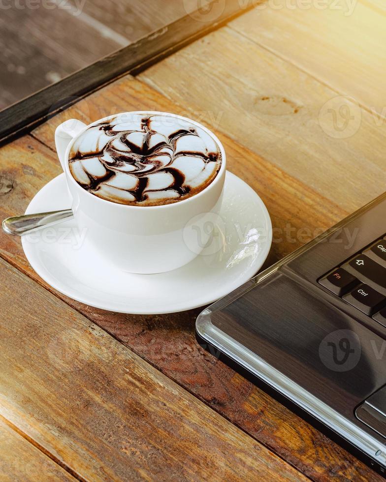 heiße Kaffeetasse und Laptop auf Holztisch im Café. foto