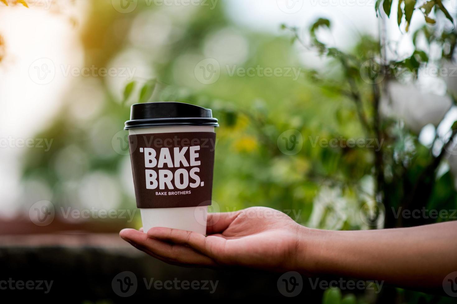 Eine Tasse Kaffee wird in die Hände und in den Boden mit einem natürlichen grünen Belagerungsraum gestellt. Bereich, der Kaffee bei der Arbeit isst weiße Kaffeetasse foto