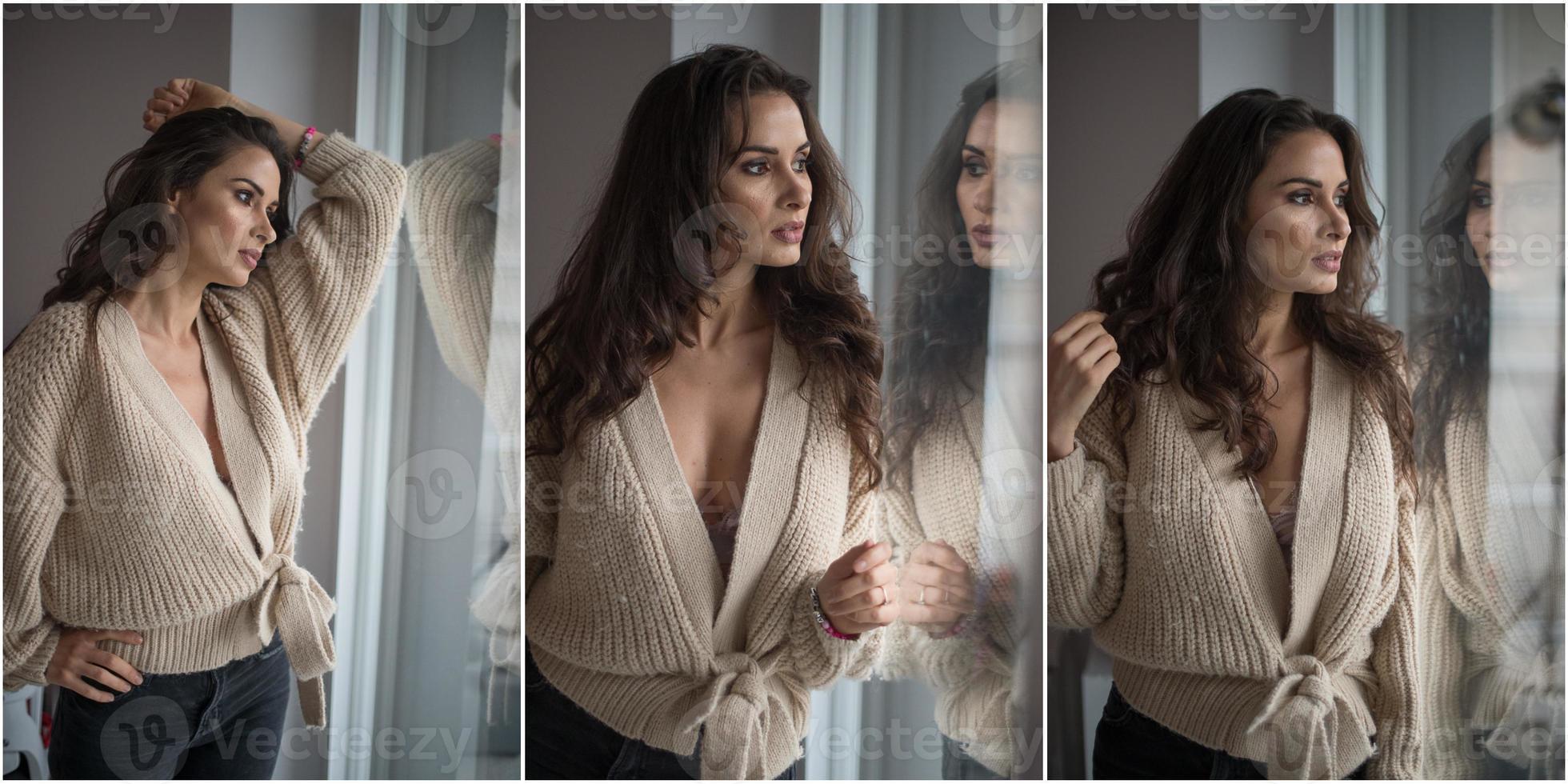 Attraktive sexy Brünette in weißem BH und braunem Pullover posiert provokativ, in der Nähe eines Fensters, Studioaufnahme. Porträt einer sinnlichen Frau mit langen Haaren, in klassischer Boudoir-Szene, schaute aus dem Fenster foto