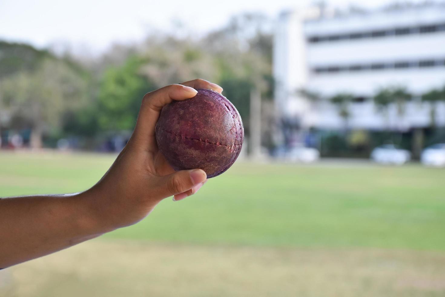 Kricketball zum Üben oder Trainieren von Hoiding in der Hand, verschwommener grüner Grasplatzhintergrund, Konzept für Cricket-Sportliebhaber auf der ganzen Welt. foto