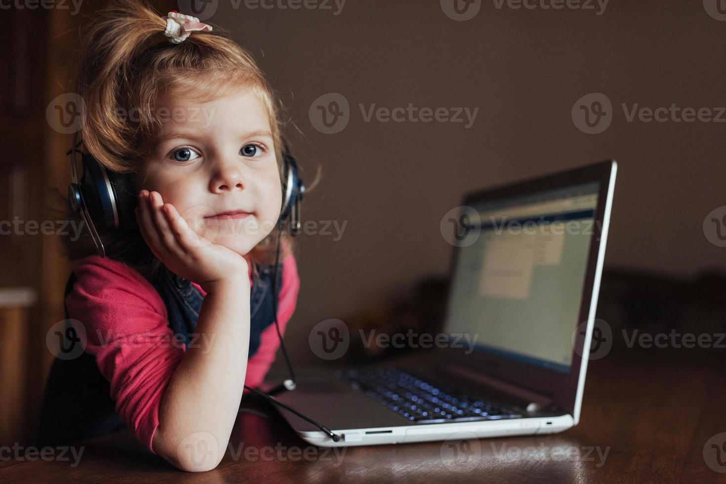 kleines mädchen mit kopfhörern, die musik hören, mit laptop foto