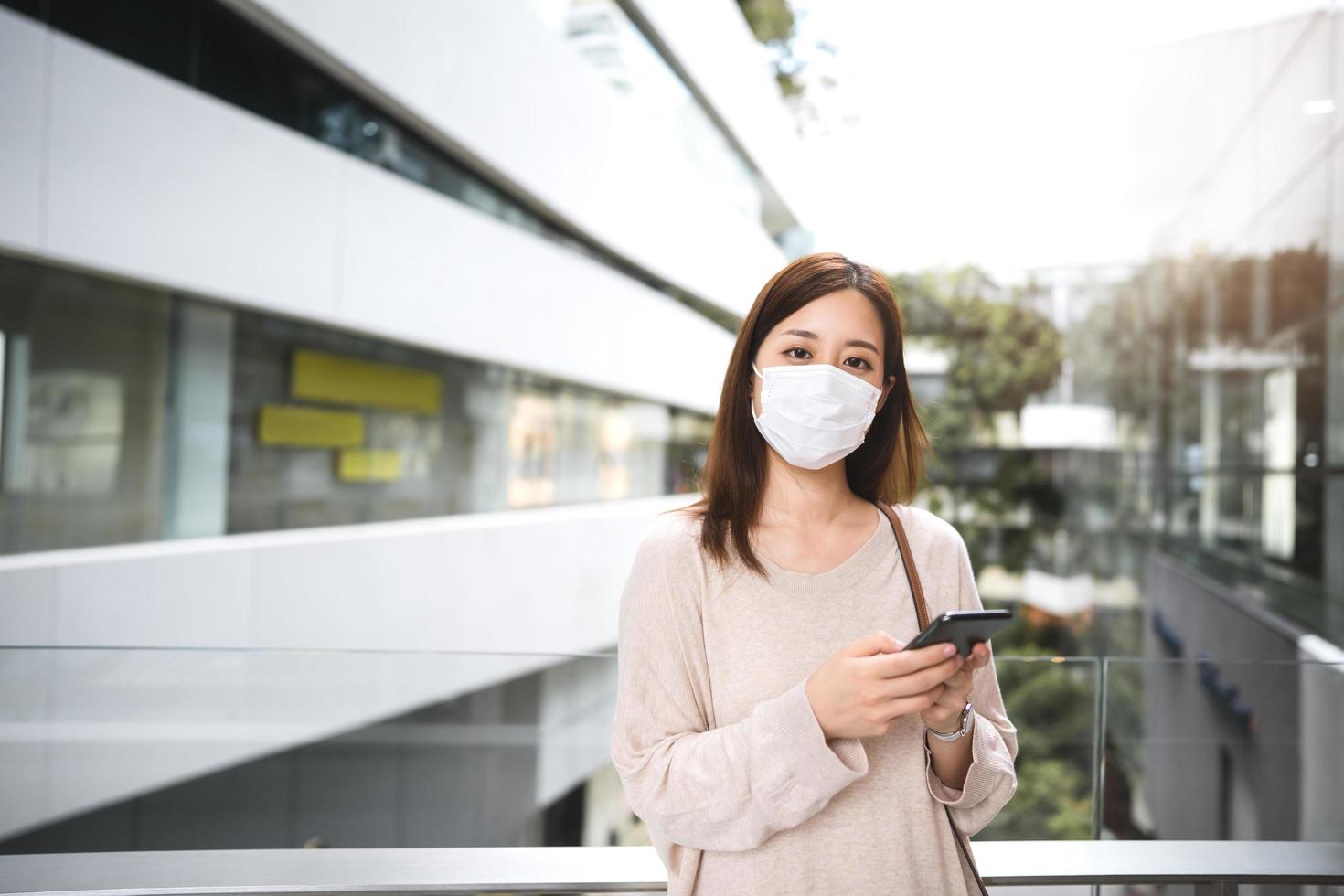 porträt einer erwachsenen asiatischen geschäftsfrau, die eine schützende gesichtsmaske für viruskorona oder covid19 mit einer mobilen app trägt foto