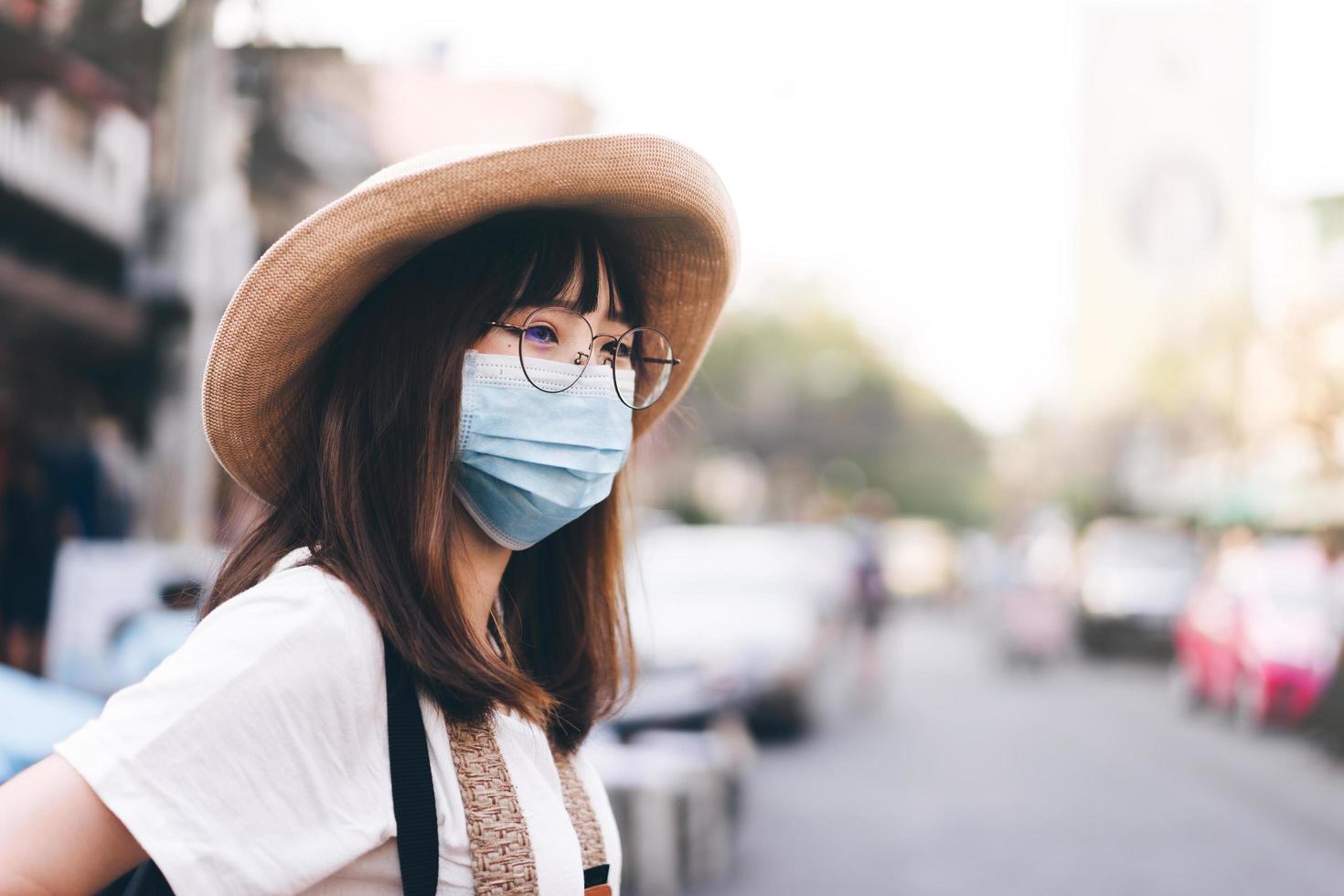 junge asiatische reisende brillenmädchen mit hut und maske schützen virus und neuen normalen lebensstil foto