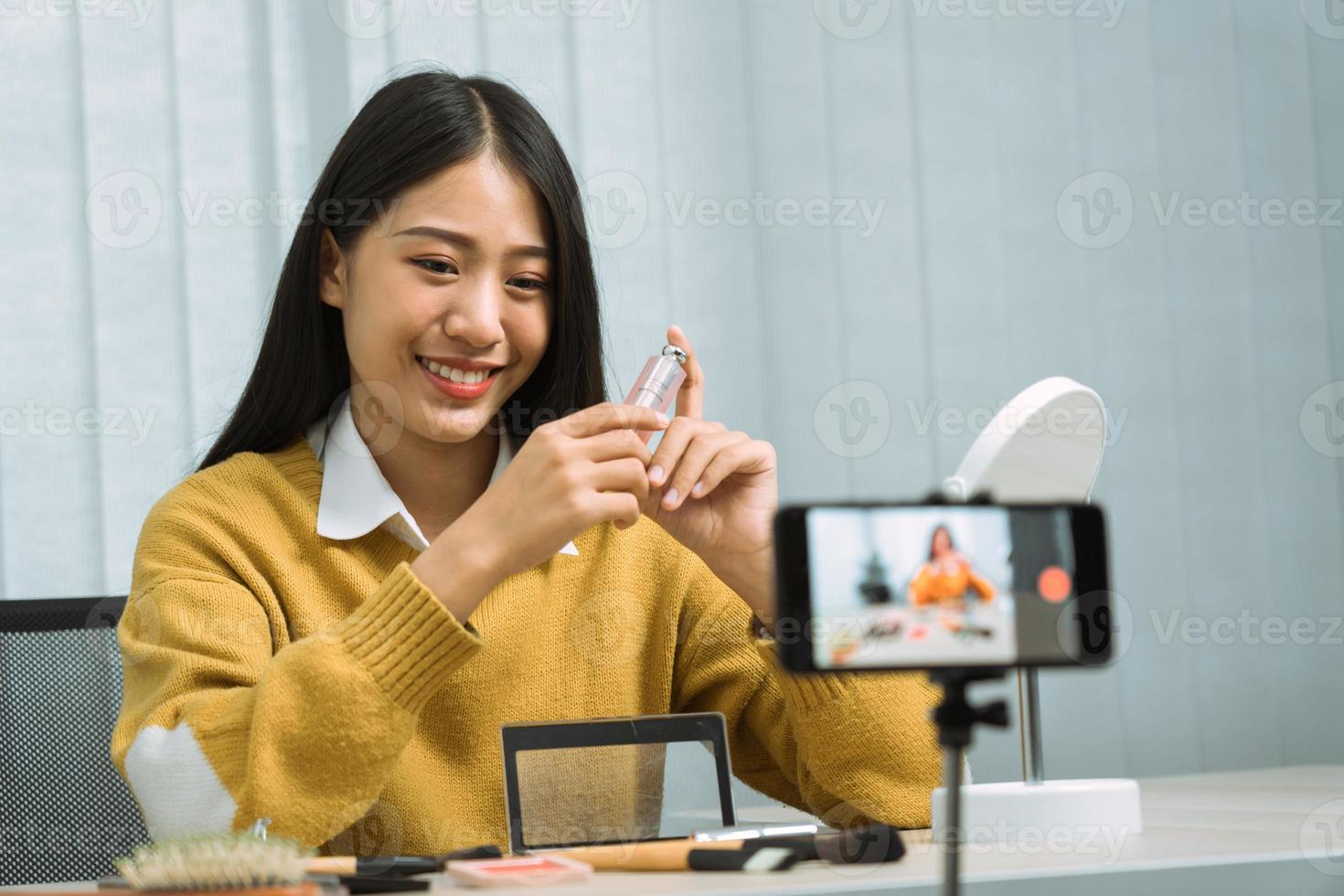 junge asiatin vloggt mit ihrer videokamera über kosmetik-hautpflegeprodukte auf dem tisch und demonstriert produktverwendung und bewertungen für ihren online-blog-kanal. foto