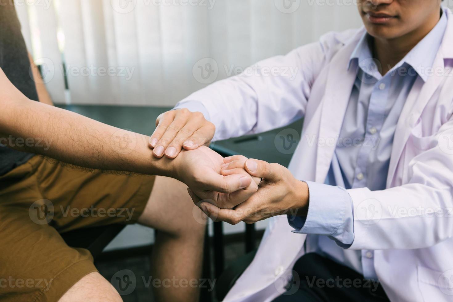 Der Physiotherapeut überprüft das Handgelenk des Patienten, indem er im Klinikraum auf den Handgelenksknochen drückt. foto
