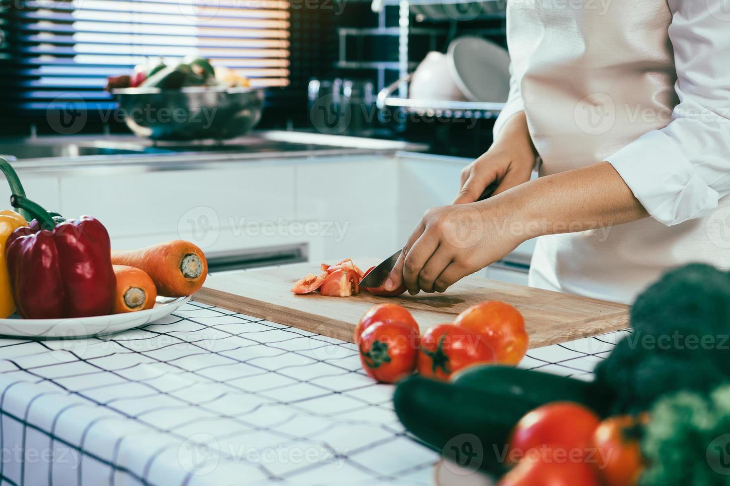 Hausfrau mit Messer und Händen schneiden Tomaten auf Holzbrett im Küchenraum. foto