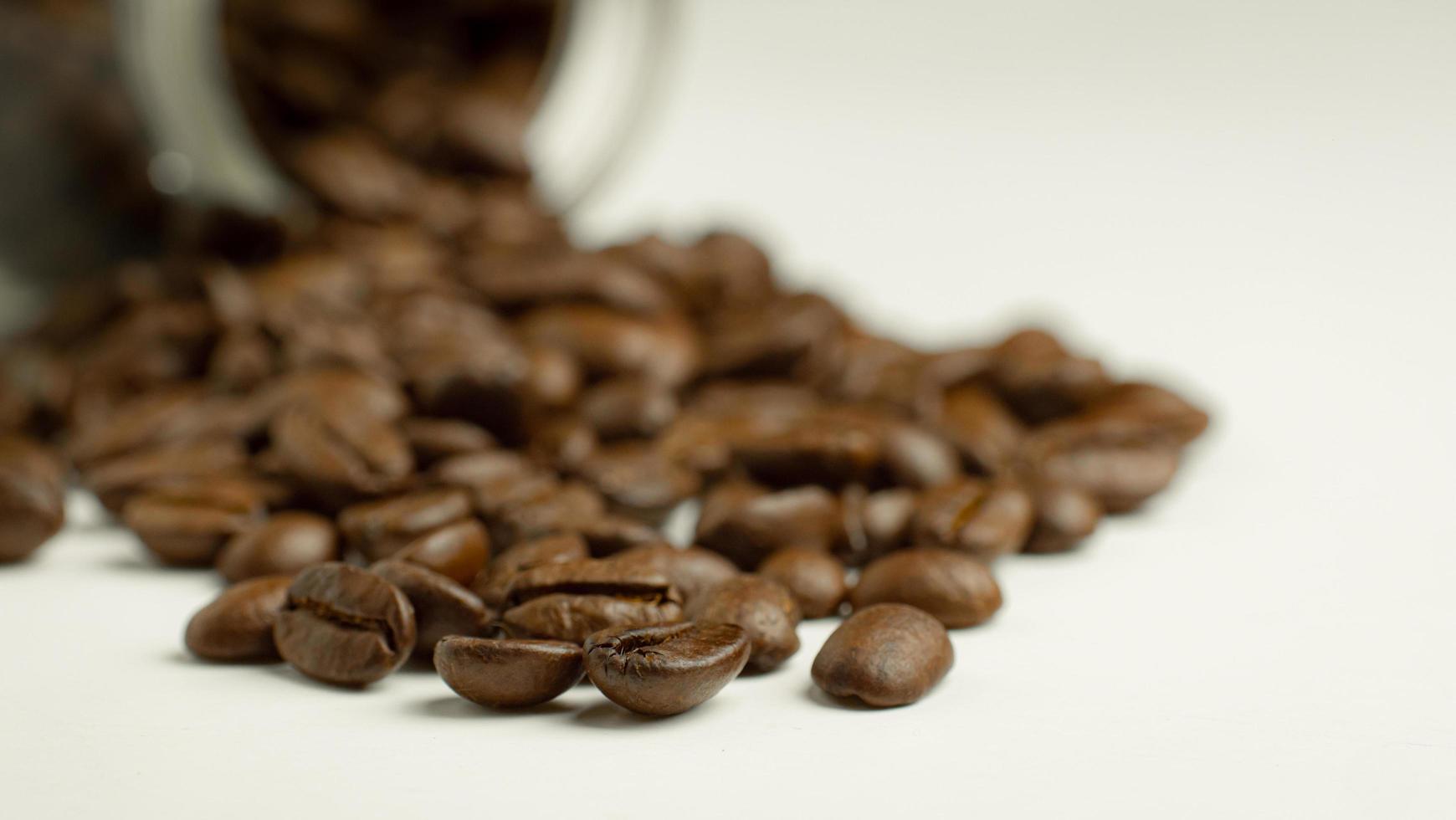 Geröstete Kaffeebohnen bereiten sich darauf vor, dass der Mahlgrad aus einer Glasflasche gegossen wird, die auf einem weißen Hintergrund liegt, um frischen Kaffee zuzubereiten oder in eine Espressomaschine oder Moka-Kanne zu gehen foto