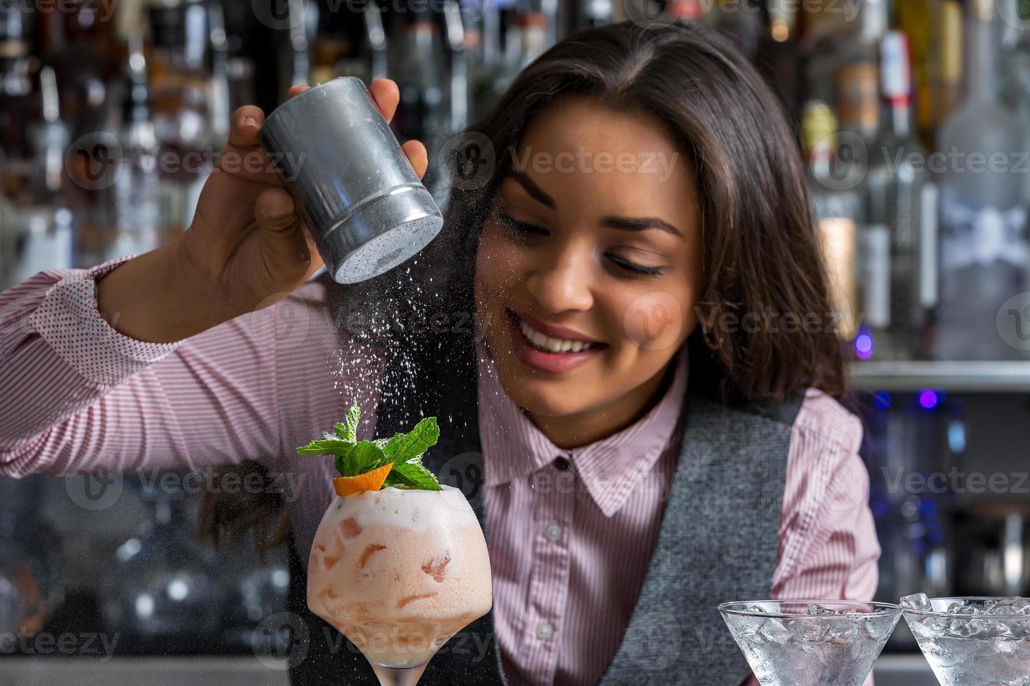 glückliche Barkeeperin, die dem Cocktail Puderzucker hinzufügt foto