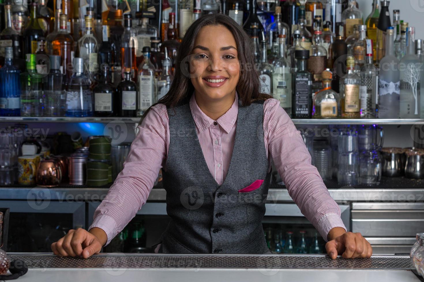 Fröhliche Barkeeperin, die hinter der Theke in der Bar steht foto