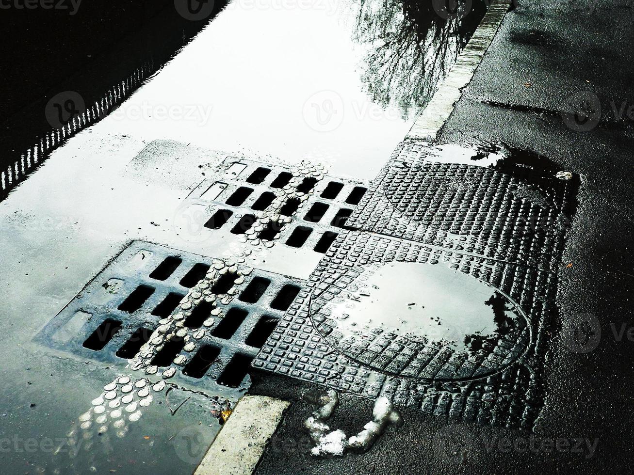 Wasser, das in den Kanalschacht fließt. Nasse Straße mit Kanalluken. foto
