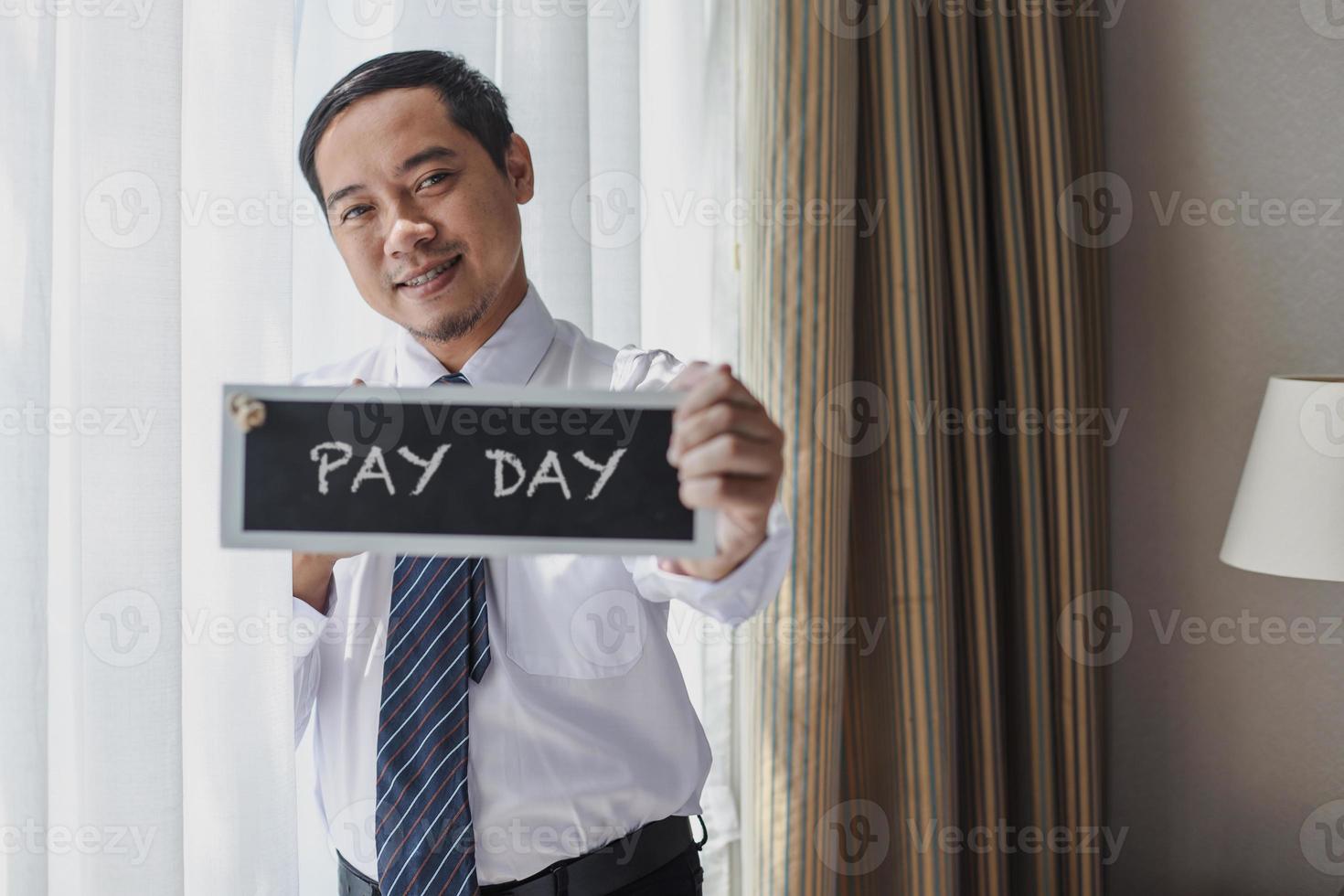 asiatischer geschäftsmann in weißem hemd und krawatte mit zahltagschild foto