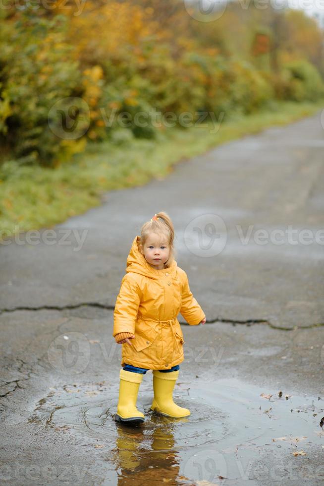 Ein kleines Mädchen geht mit einem Regenschirm in gelben Gummistiefeln und einem wasserdichten Regenmantel spazieren. Herbstspaziergang. foto