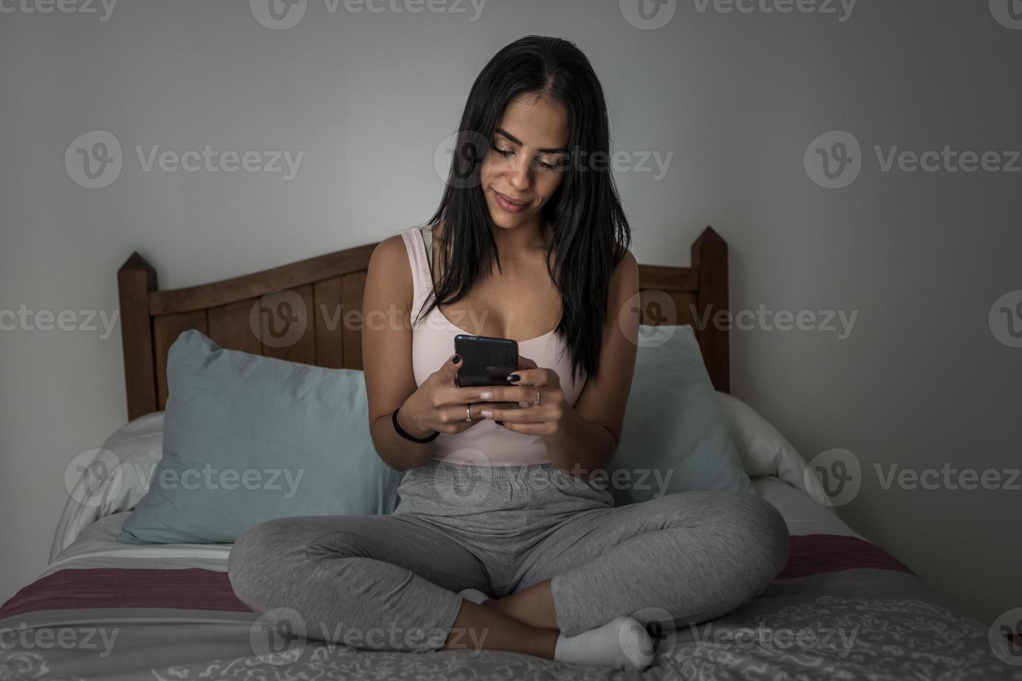 Zufriedene Frau, die abends Smartphone auf dem Bett benutzt foto