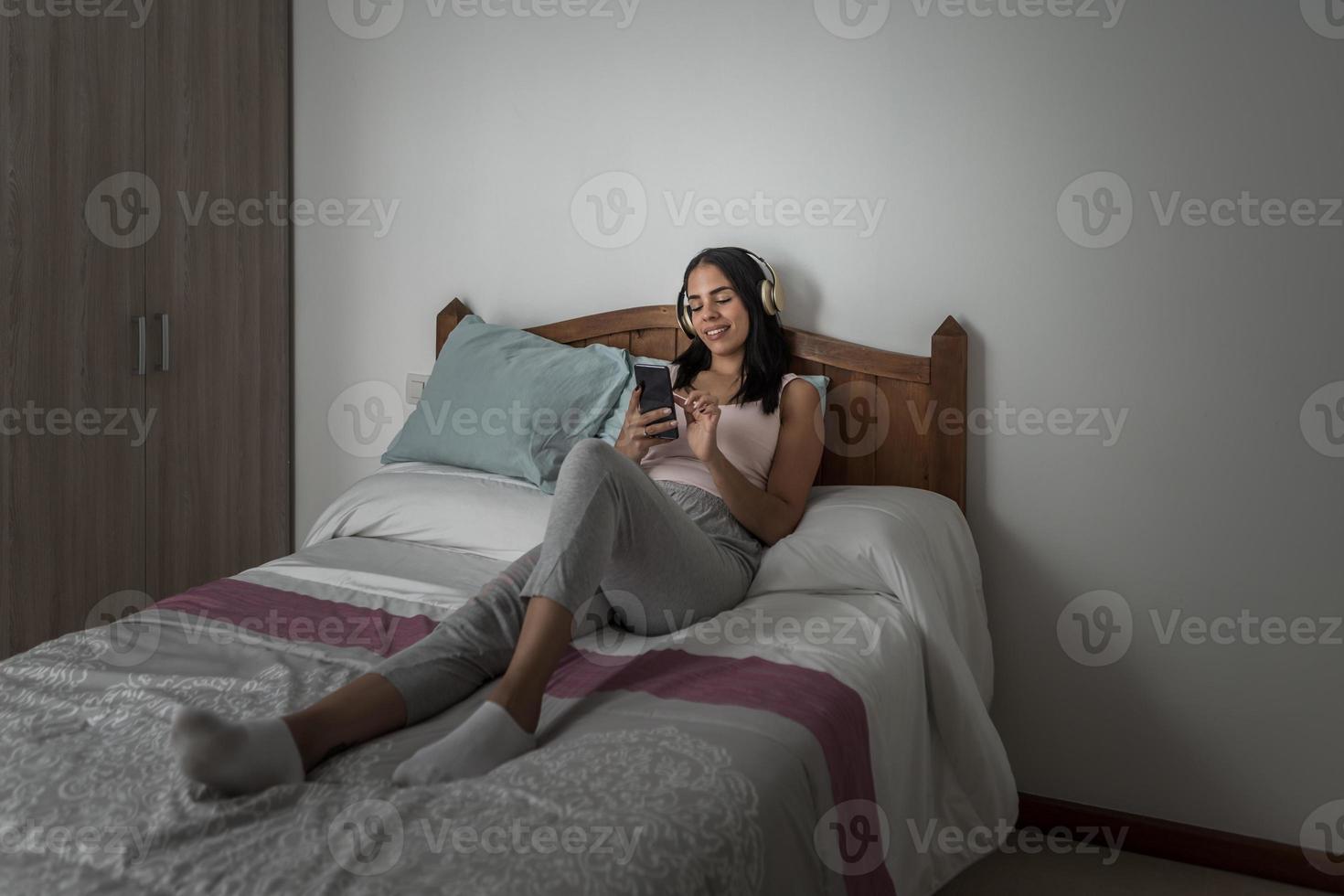 Zufriedene Frau, die Musik hört und Smartphones auf dem Bett durchsucht foto