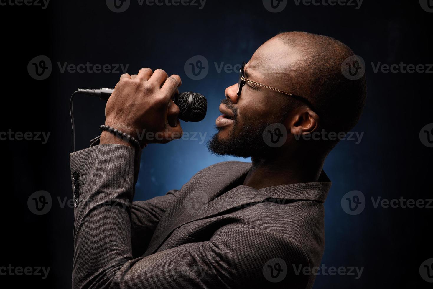 Ein schwarzer Afroamerikaner singt emotional in ein Mikrofon. Nahaufnahme Studioporträt. foto
