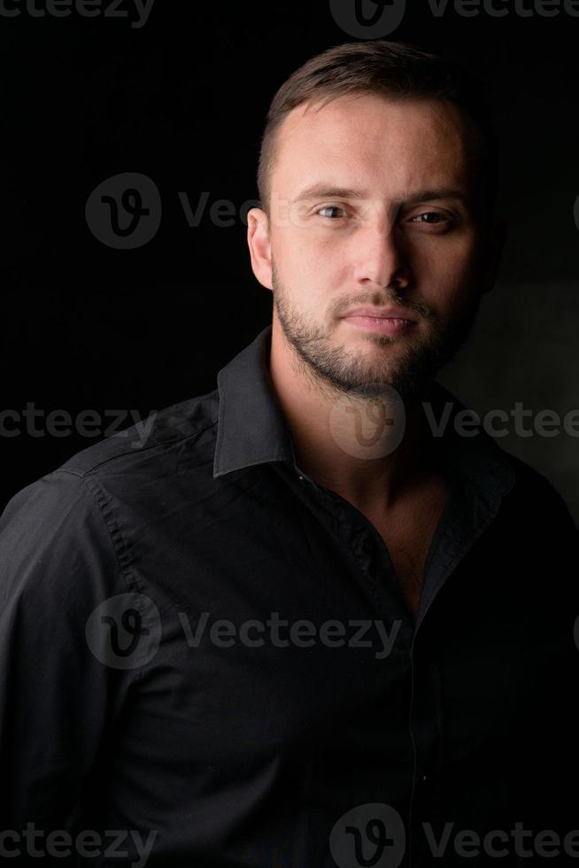 Studioporträt eines jungen kaukasischen Mannes in einem schwarzen Blazer, der die Kamera anschaut und vor einem schlichten Studiohintergrund steht foto