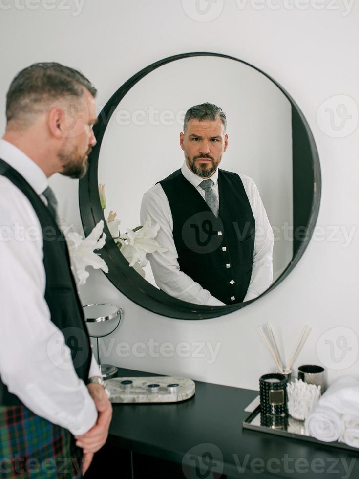 hübscher reifer mutiger stilvoller mann schotte im anzug am spiegel. stil, mode, lebensstil, kultur, ethnisches konzept. foto
