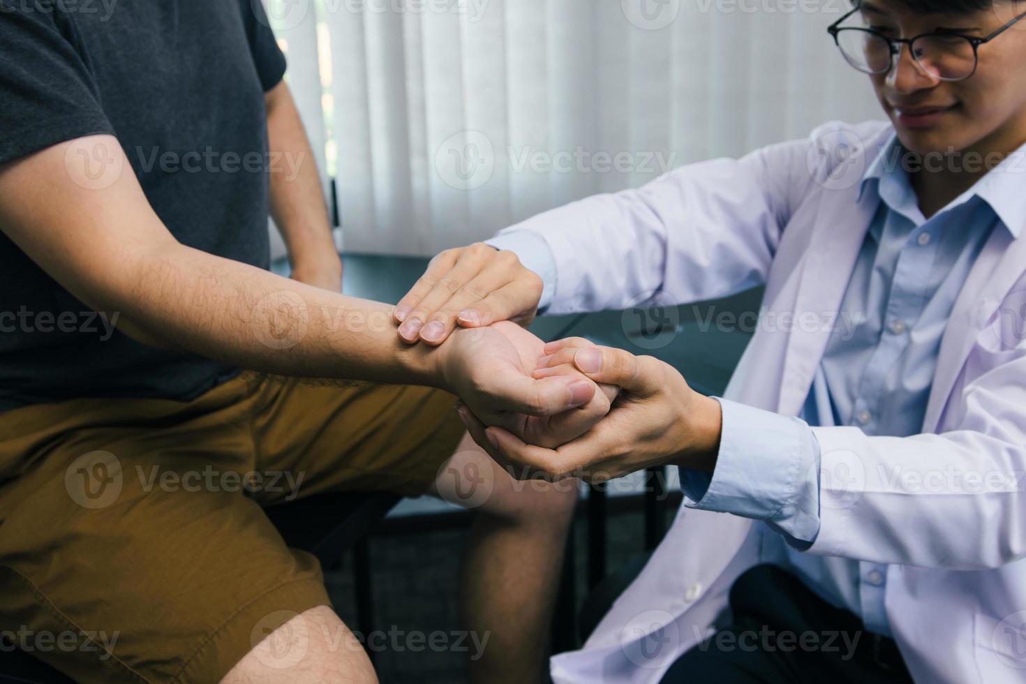 Der Physiotherapeut überprüft das Handgelenk des Patienten, indem er im Klinikraum auf den Handgelenksknochen drückt. foto