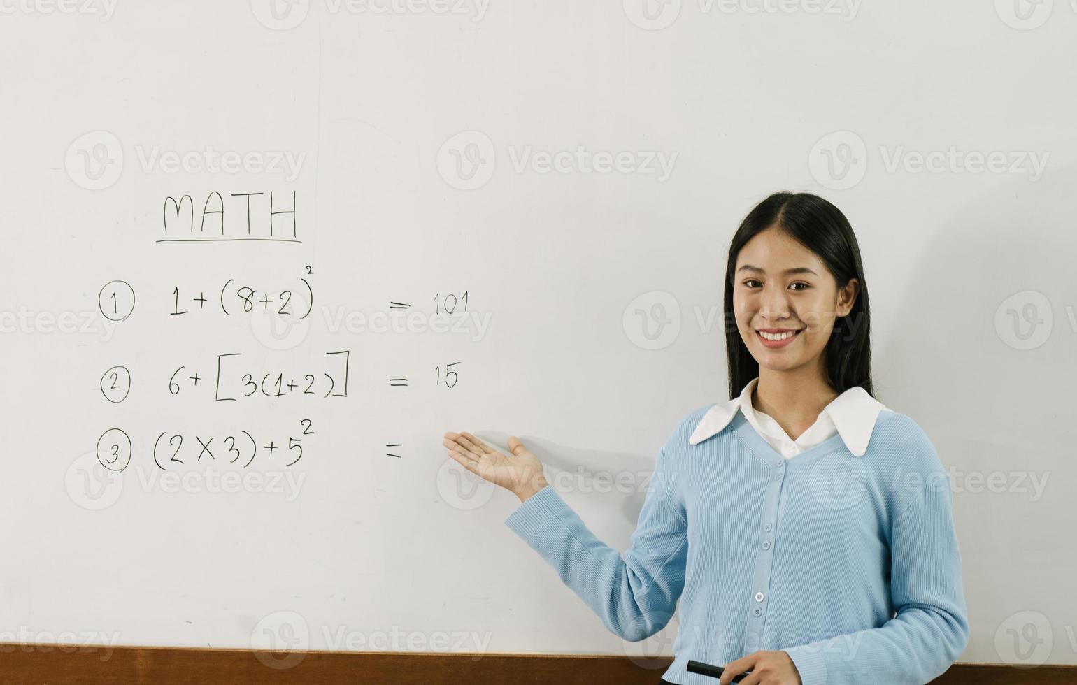 asiatische lehrerin unterrichtet schüler im klassenzimmer, während sie auf zahlen auf der weißen tafel zeigt. foto