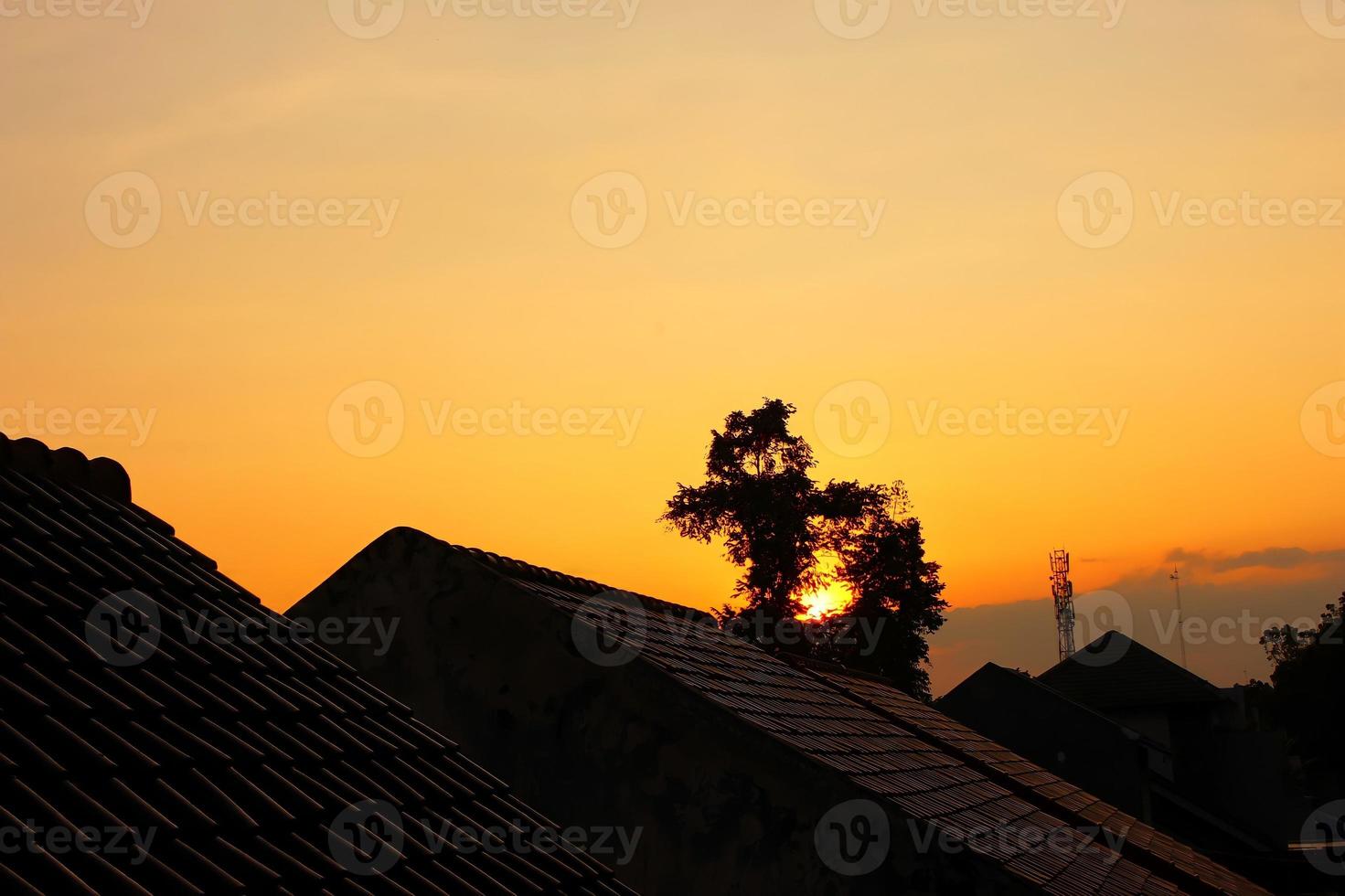 Fotos von Dächern, Bäumen und anderen Häusern am Nachmittag, wo der Himmel orange ist, kann dieses Foto ein besonderes Gefühl für diejenigen hervorrufen, die es sehen