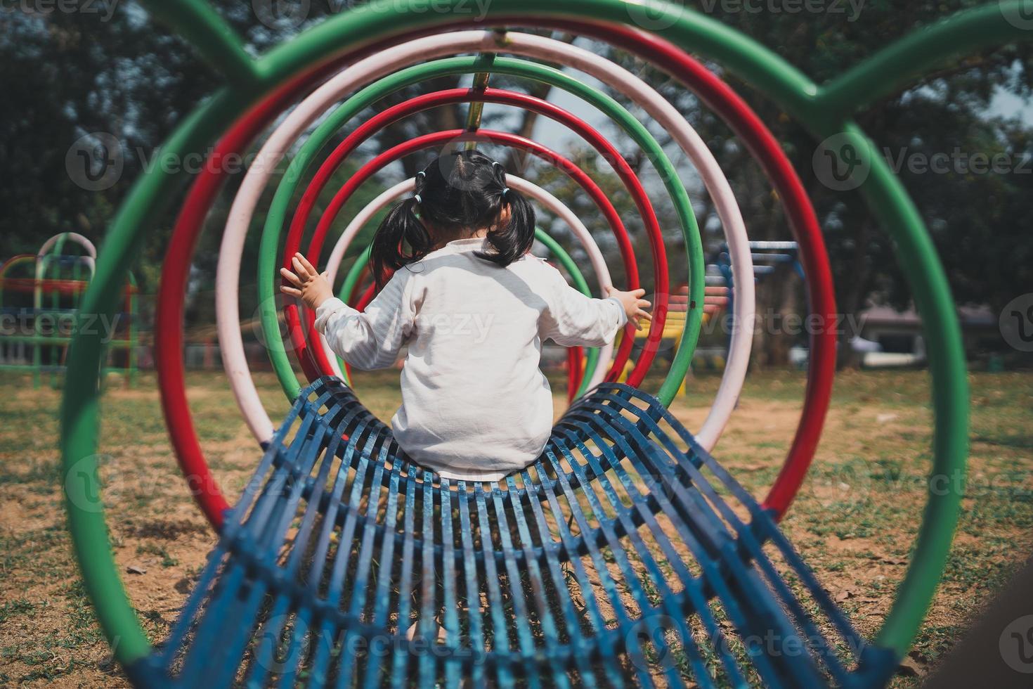 süße asiatische mädchen spielen auf dem hof der schule oder des kindergartens oder auf dem spielplatz. gesunde sommeraktivität für kinder. Kleines asiatisches Mädchen, das draußen auf dem Spielplatz klettert. Kind spielt auf Spielplatz im Freien. foto