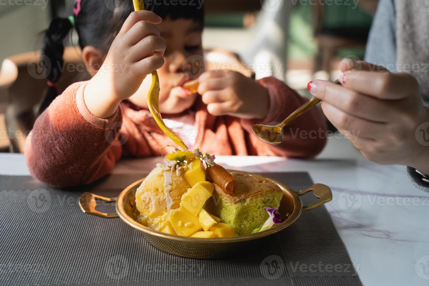 Mutter füttert ihre kleine Tochter. glückliches kleines Mädchen, das Eis mit Mutter im Wohnzimmer isst. Familie Happy Food Kleinkind Konzept foto