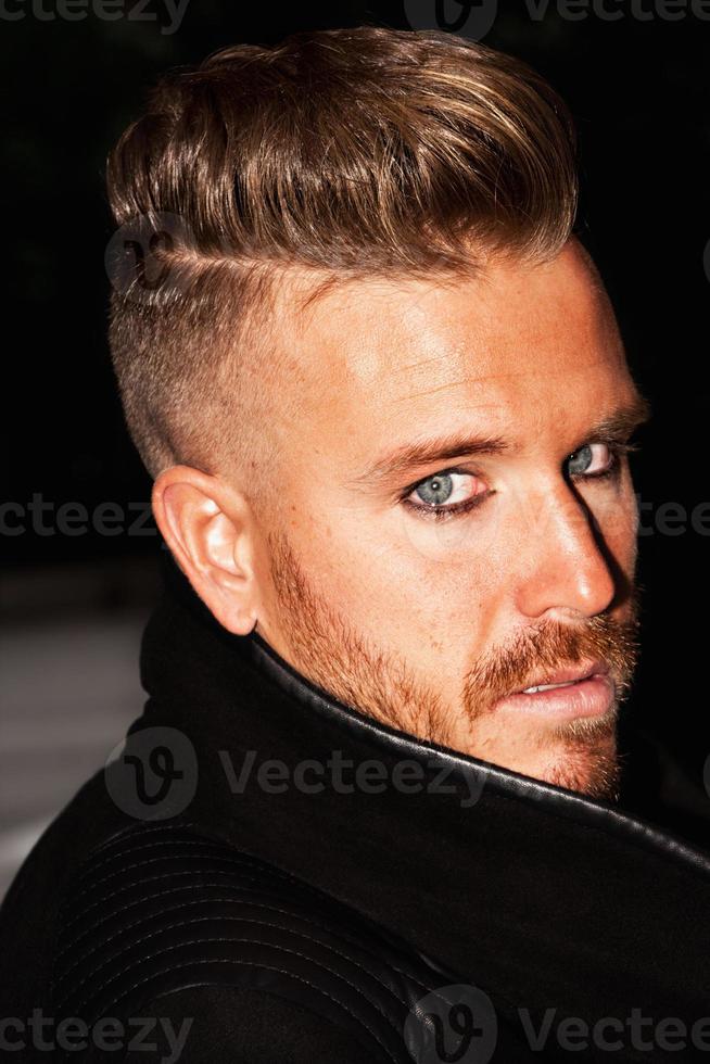 Porträt eines modischen jungen Mannes mit blauen Augen, stylischem Haarschnitt und posiert mit einer schwarzen Jacke. Nahansicht. vertikales Bild. foto