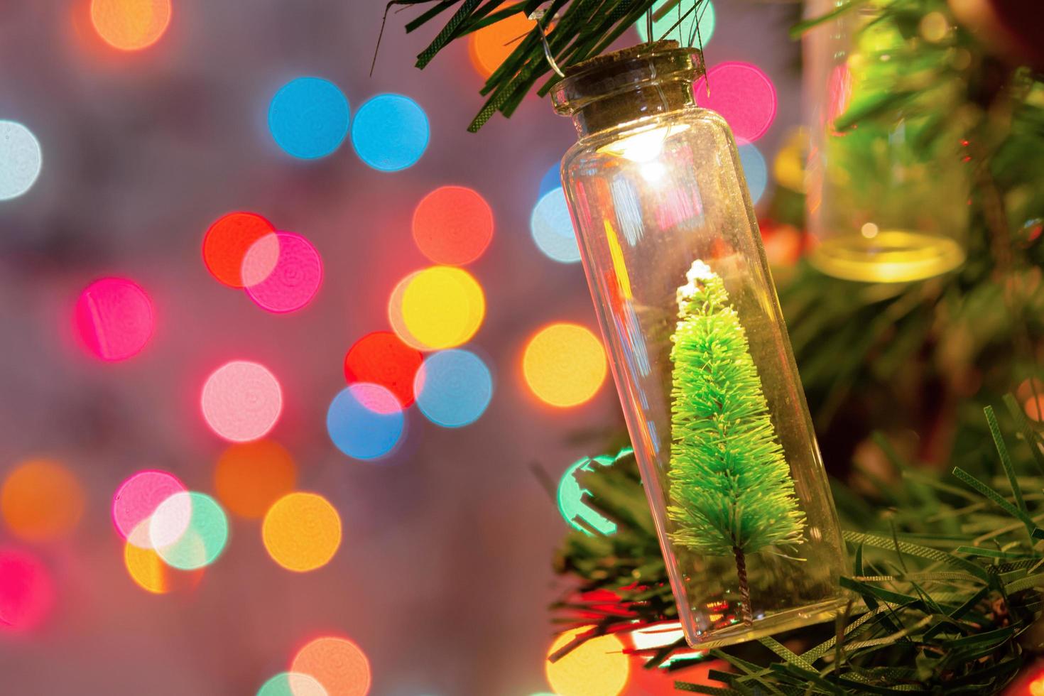 Frohe Weihnachten und ein glückliches Neues Jahr. hängender kleiner weihnachtsbaum im glas auf tannenzweigen weihnachtsbaumgirlande und verzierungen über abstraktem bokeh foto