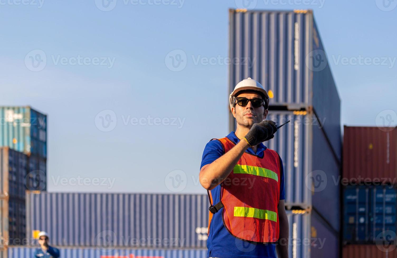 ingenieur in helm und sicherheitsweste mit funkgerät, werkarbeiterteam am frachtcontainer foto