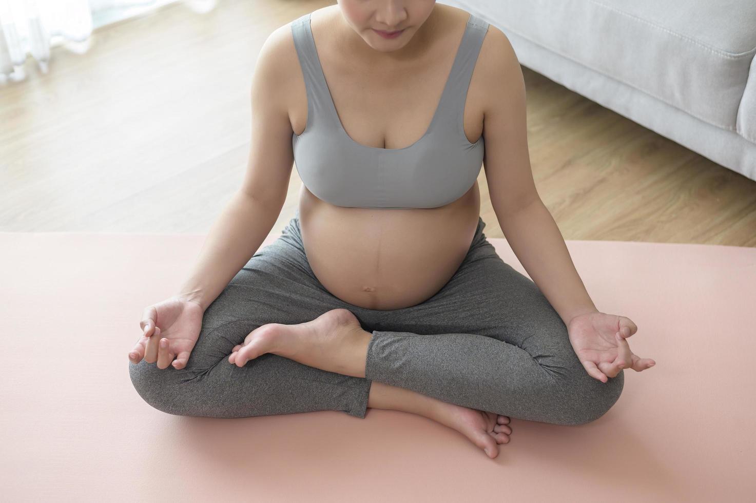 junge schwangere frau, die zu hause yoga macht, gesundheits- und schwangerschaftspflegekonzept foto