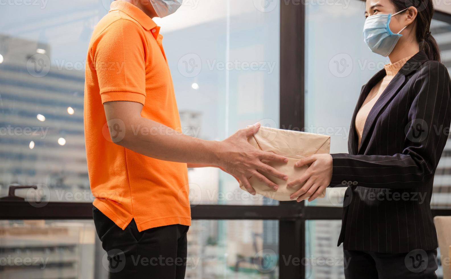 frau trägt gesichtsmaske, die paket vom zustelldienst erhält, junge lieferangestellte in t-shirt uniform trägt gesichtsmaske foto