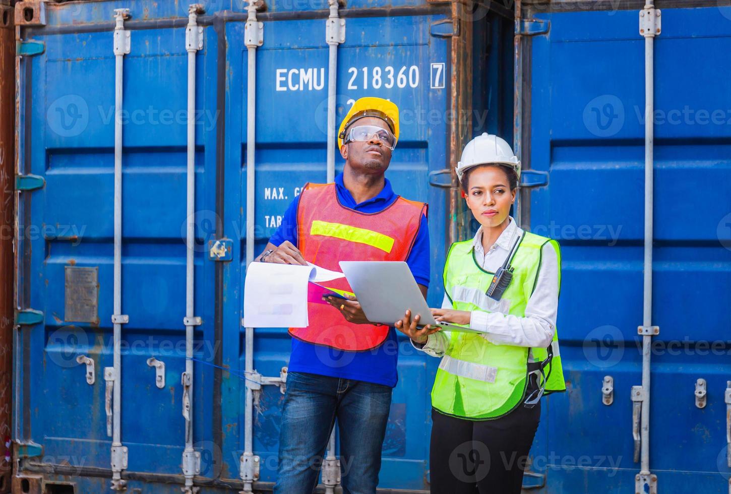 arbeitermann in helm und sicherheitsweste, der klemmbrett-checkliste hält, und weiblicher vorarbeiter, der laptop-steuerung verwendet, um containerbox von der fracht zu laden foto