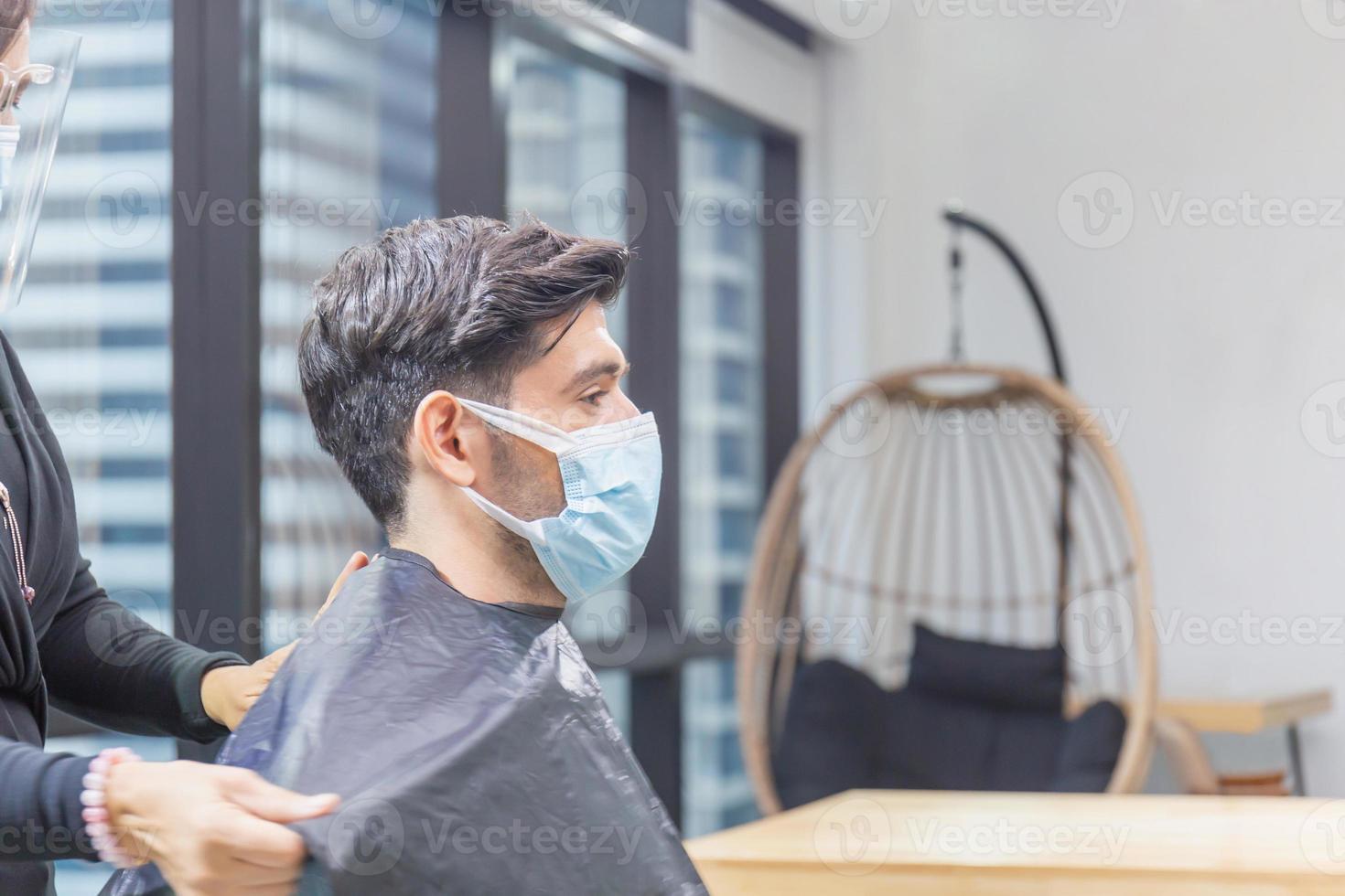 junger mann, der sich vom friseur die haare schneiden lässt, friseur mit schere und kamm, neue normale konzepte foto