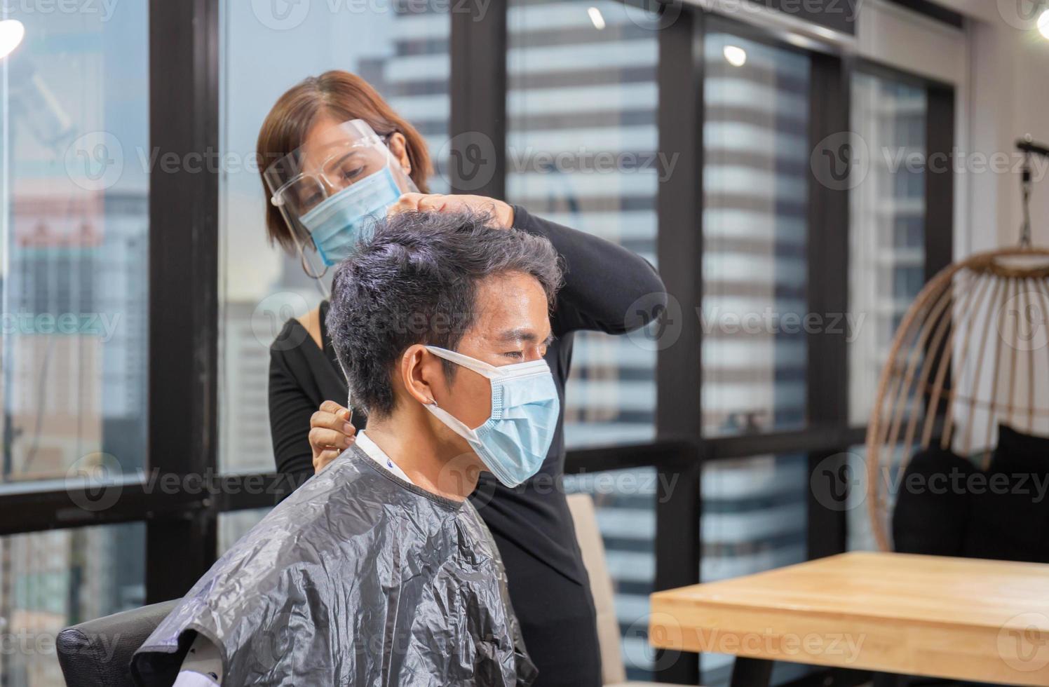 junger mann, der sich vom friseur die haare schneiden lässt, friseur mit schere und kamm, neues normales konzept foto